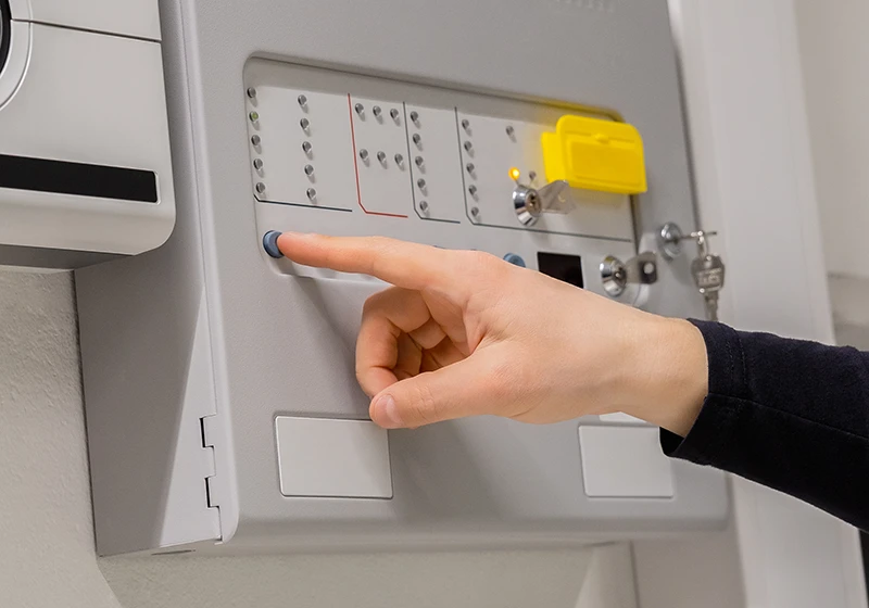 A person pressing a button on a fire alarm panel