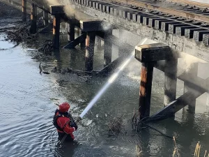 A swift water firefighter spraying water on a train track fire